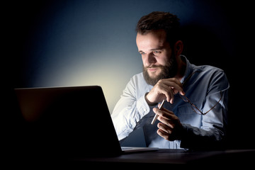 Young handsome businessman working late at night in the office with a dark background