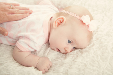 Calm baby lying on stomach with mothers hand on back