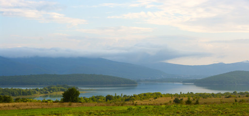 Obraz premium Lake in valley among foggy mountains