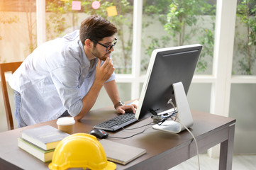 Engineers working within an office using a computer. He put the helmet on the side