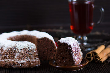 Piece of christmas chocolate sponge cake with sugar powder on wooden table with glass of red tea and sticks of cinnamon