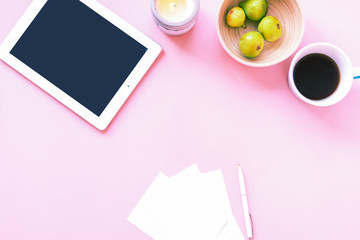 Woman desktop with tablet computer, coffee and green figs in a bawl on pink background. Planning concept, top view, flat lay.