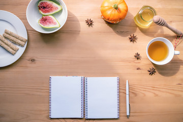 Autumn flat lay with notebook, pen, hot tea, honey, pumpkin, figs and sesam bars on white plate. Planning concept.