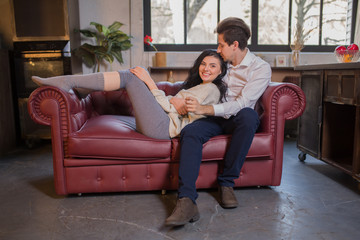 Obraz premium Happy Girl in Embrace looks Guy looks at him with an apple in his hands on the sofa in the kitchen