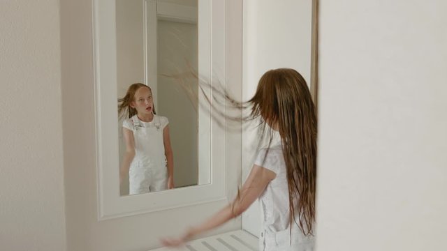 Teenager girl looking wet hair front mirror in bedroom. Young girl with wet hair after shower posing front bathroom in home back view