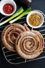 Metal cooling rack with grilled coiled sausages, ketchup and dijon mustard, vertical shot, close-up
