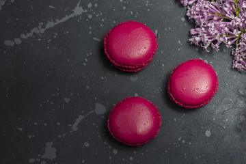 Colorful french macarons cookies(macaroons) with lilac branch of on a dark background with copy space.