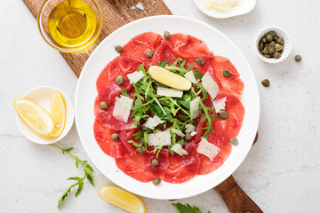 Beef Carpaccio cold appetizer with parmesan, capers and arugula on white plate.Top view.