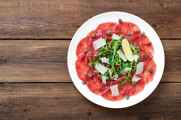 Beef Carpaccio cold appetizer with parmesan, capers and arugula on white plate.Top view.