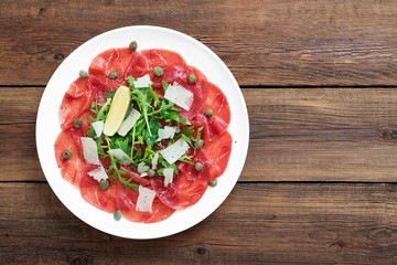 Beef Carpaccio cold appetizer with parmesan, capers and arugula on white plate.Top view.