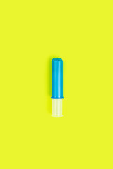 Aqua blue plastic tampon applicator isolated on bright neon yellow background