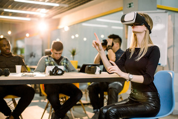Young Caucasian woman in VR goggles at a desk with colleagues in an office