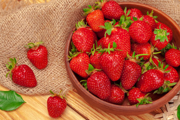 Bowl of strawberry harvest on wooden table close up