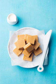 Fresh caramel fudge candies on a plate. Blue background. Top view.
