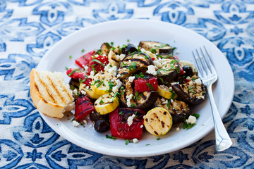 Grilled vegetables salad with feta cheese in white plate on blue textile background. Close up.