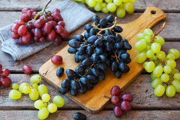 Assortment fresh grape on cutting board. Grey wooden background.