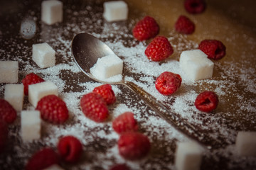 berries of red raspberries with a teaspoon and cubes of refined sugar lie on a wooden rustic table top view