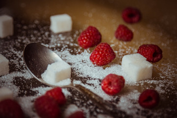 berries of red raspberries with a teaspoon and cubes of refined sugar lie on a wooden rustic table top view