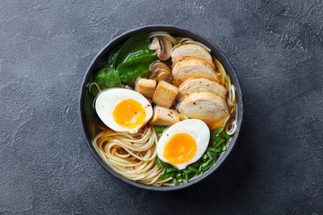 Asian noodle soup, ramen with chicken, tofu, vegetables and egg in black bowl. Top view. Copy space. Slate background.