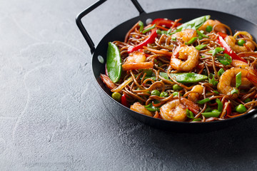 Stir fry noodles with vegetables and shrimps in black bowl. Slate background. Copy space.
