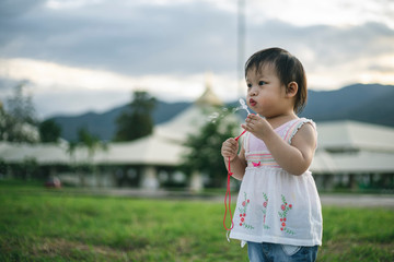Little child girl playing with bubbles on green grass outdoors in the park.