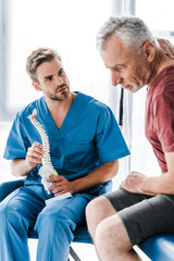 selective focus of doctor holding spine model and looking at patient