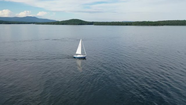 Aerial video of small white sailboat yacht on lake in New England summer