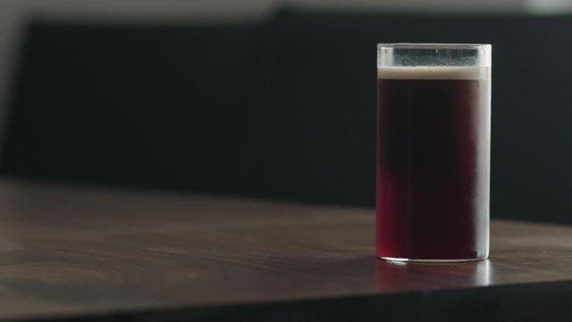 Slow motion man takes nitro coffee in glass from walnut table