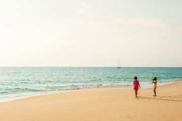 Two asian girls relaxing on the sunset beach with digital camera.