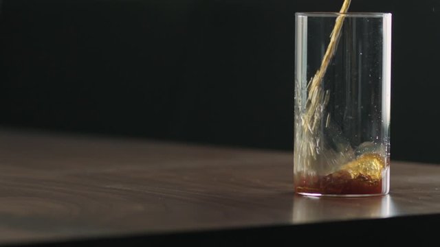 Slow motion pour nitro coffee into glass on walnut table