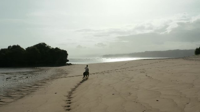 Drone shot of a child bareback riding a horse on a sandy beach, near Ratenggaro Village, Sumba, with the ocean in the background