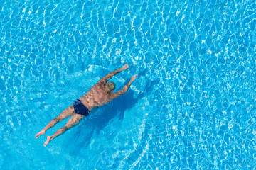 A man swims underwater in a transparent pool.