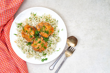 Stewed meatballs and rice in a white plate with herbs on a gray table