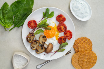 Fried eggs, tomatoes, mushrooms with spinach, microgreen, bread chips and sauce on a white plate