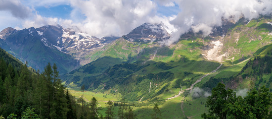 Green valleys, high firs and snow-covered mountains in clouds, Austria