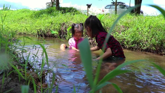 Children playing  barefoot in stream water, play mud and sand.