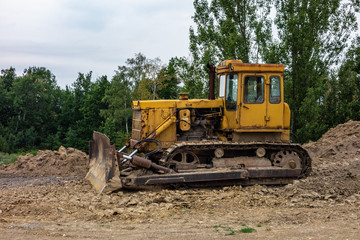 A yellow bulldozer on a constrction site preparing a terrain in order to build a new building