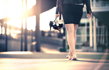 Woman holding high heels in hand and walking home from party barefoot. Businesswoman took off...