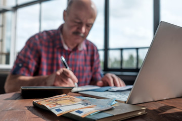 Serious mature hispanic man man checking home finance calculating money. Focus on euro money.