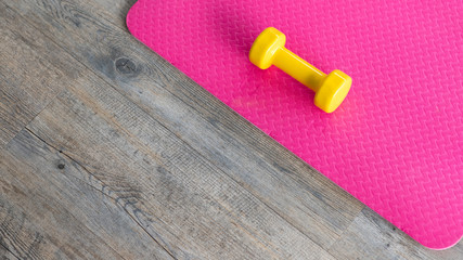 Fototapeta na wymiar yellow dumbbells on an empty pink rubber floor on wooden floor background,top view with copy space health and exercise concept