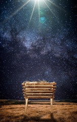 Vertical shot of an old wooden cradle with hay in a field and under a beautiful starry sky
