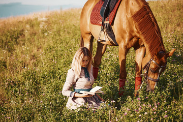 girl reading a book in the field next to a horse