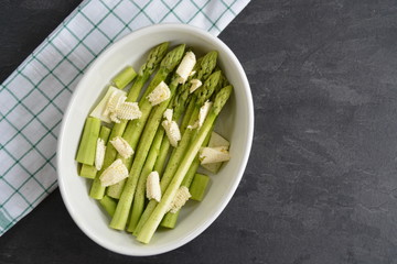Green fresh peeled asparagus with pieces of butter and spices in a porcelain bowl, ready to be put in the oven
