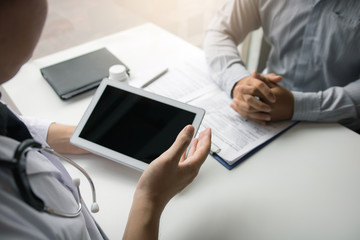 Asian doctor talking the patient at clinic while using the tablet explaining the patient condition and the treatment result.