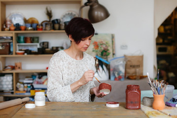 Caucasian craftswoman enamels clay cup in workshop