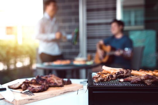 Close up grilled meats and various food on the grill and celebrations of friends who are playing guitar and sing together in their home.