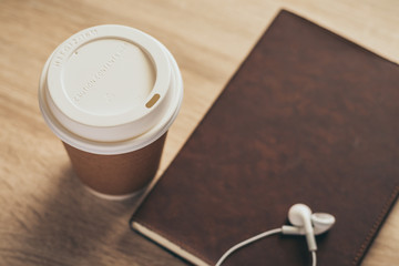 Brown paper cup of coffee with textbook or diary with headphones on wood desk with copy space. Photo concept of branding ,cafe, leisure, reading, refreshment, relaxation. Food and beverage image