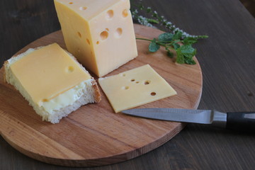 Cheese with holes lies on a wooden board on a brown table.
