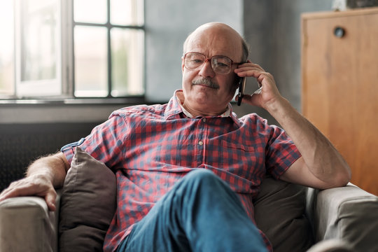 Retired Hispanic Man Talking On Phone Sitting At Living Room. Discuss Important Questions.