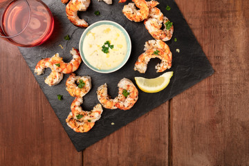 Fried shrimps with a Caesar sauce and lemon, shot from above on a dark rustic wooden background with a glass of rose wine and copy space